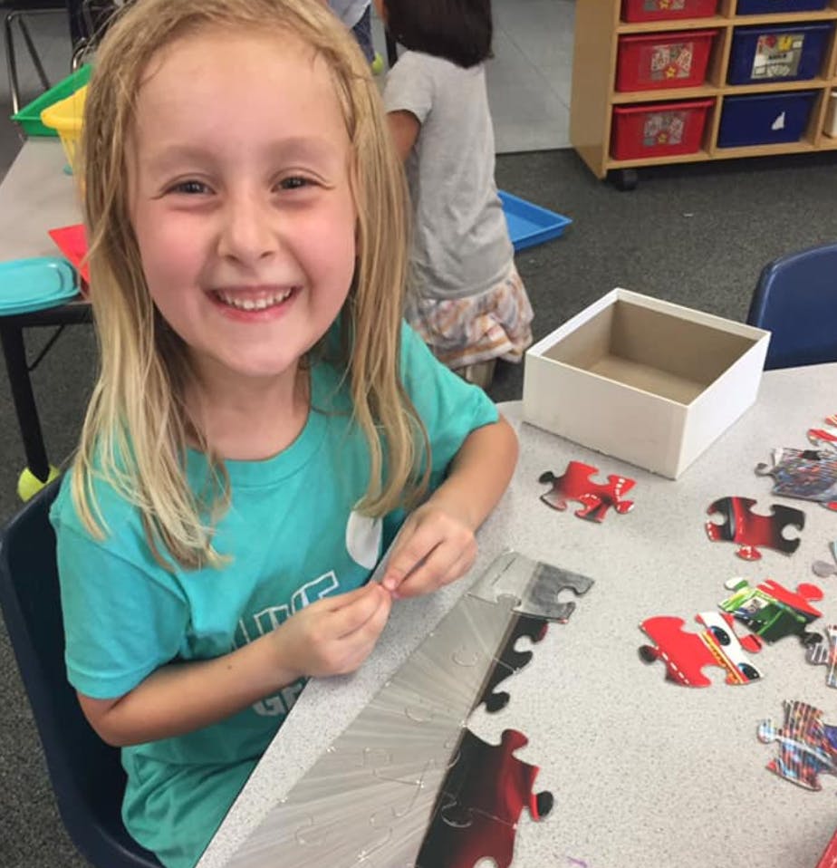 Child smiling while working on a puzzle at a table with puzzle pieces