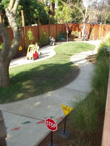 Children playing in a backyard with a winding path and toy cars