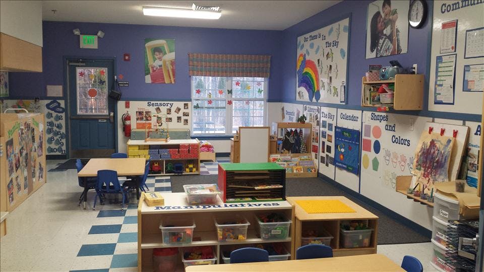 Empty classroom with small tables and chairs, toys, and educational posters on the walls