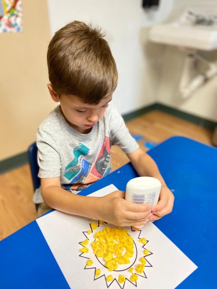 Child gluing yellow pieces onto a sun drawing