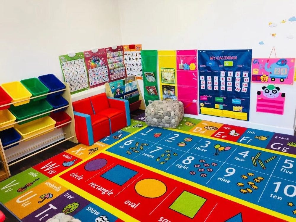 Colorful classroom with a number and shape rug, small red couch, and wall charts