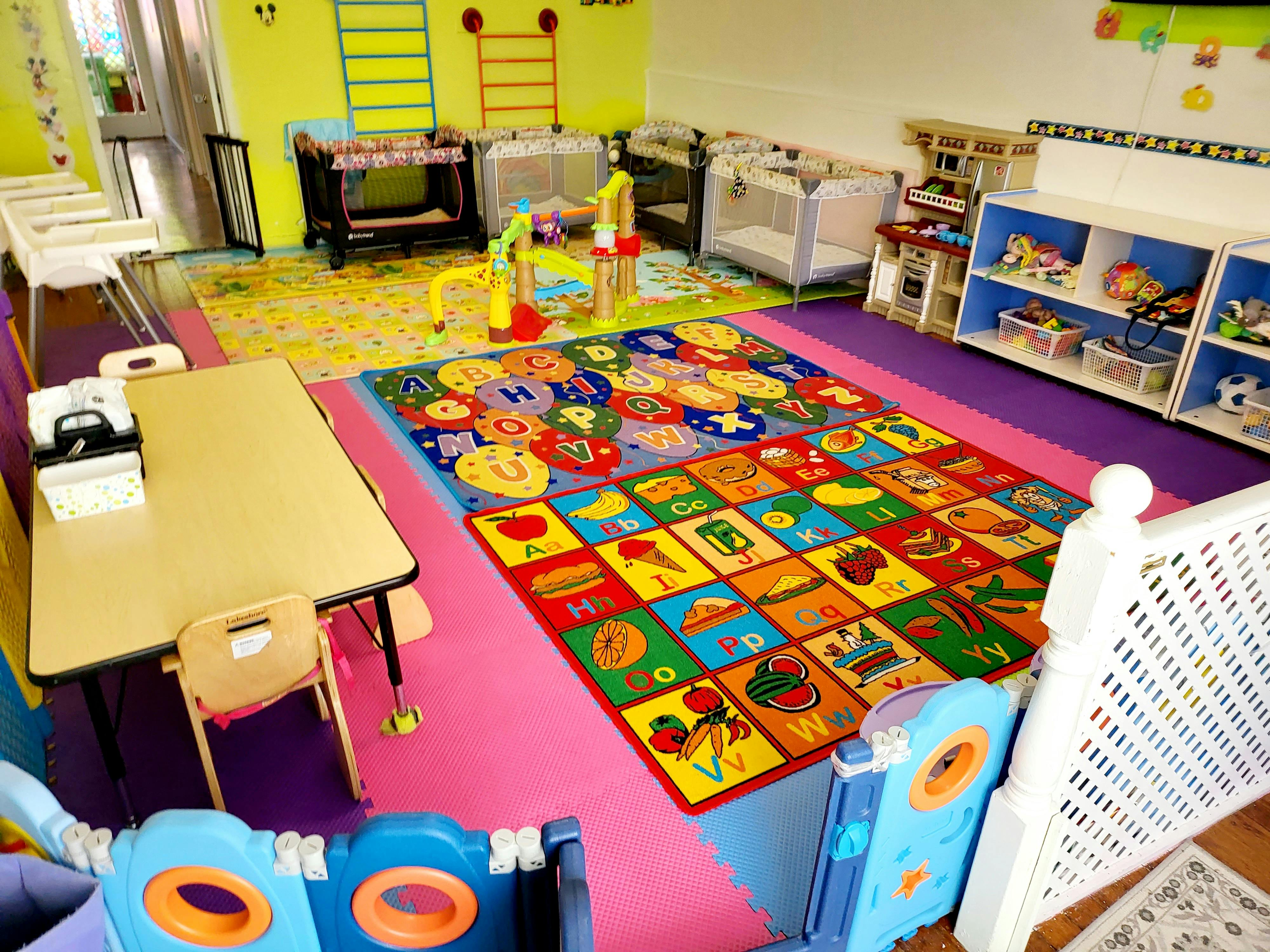 Colorful play area with alphabet rug, small tables, and cribs