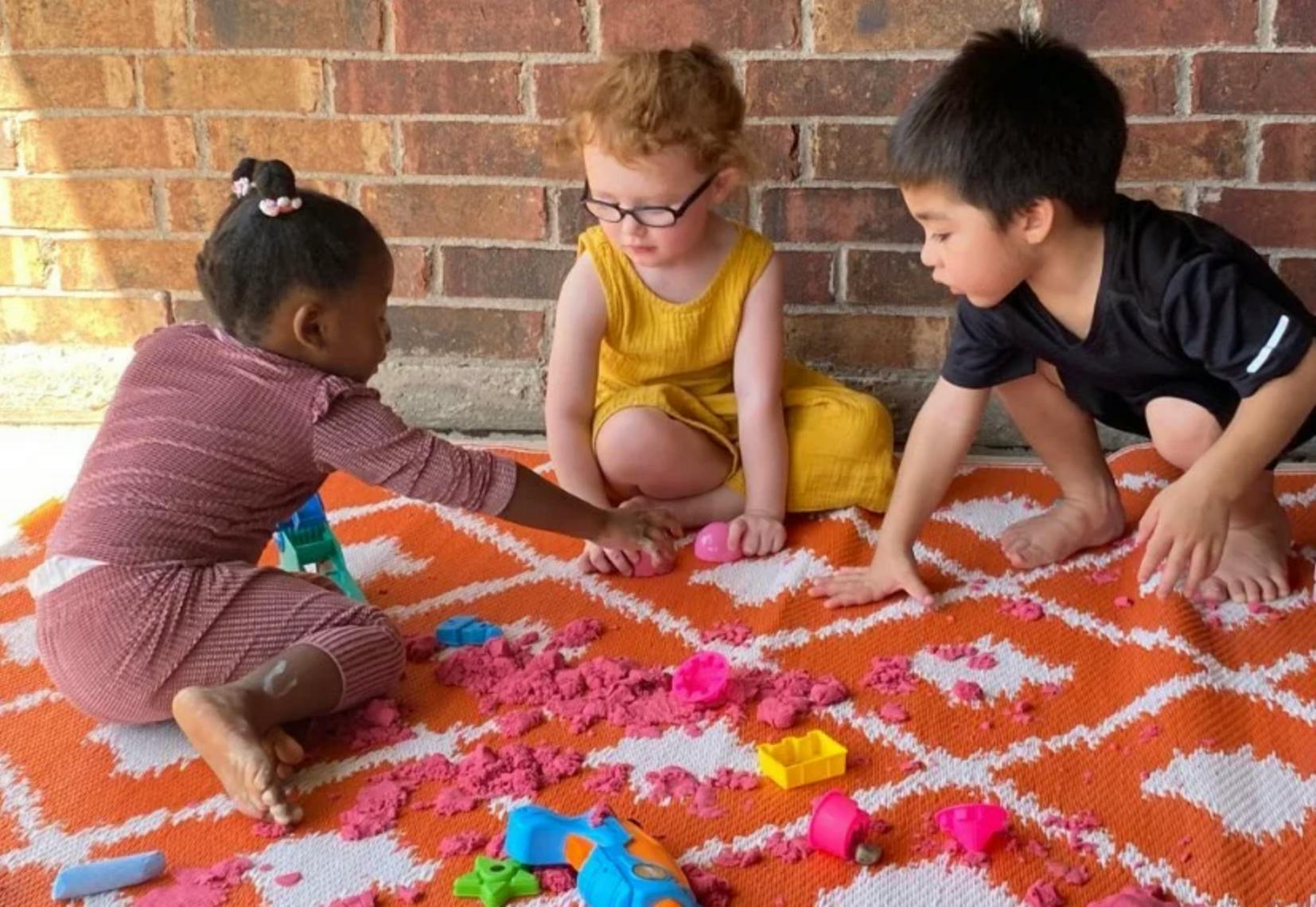 Three children playing with kinetic sand on a mat