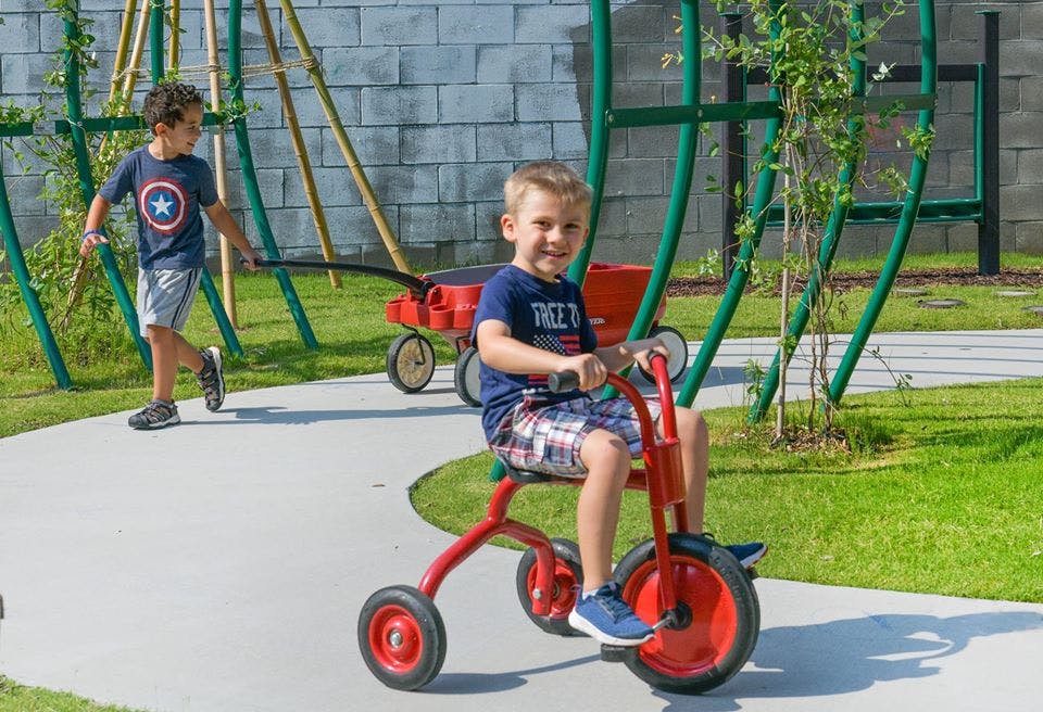 Child on a red tricycle and another child pulling a red wagon
