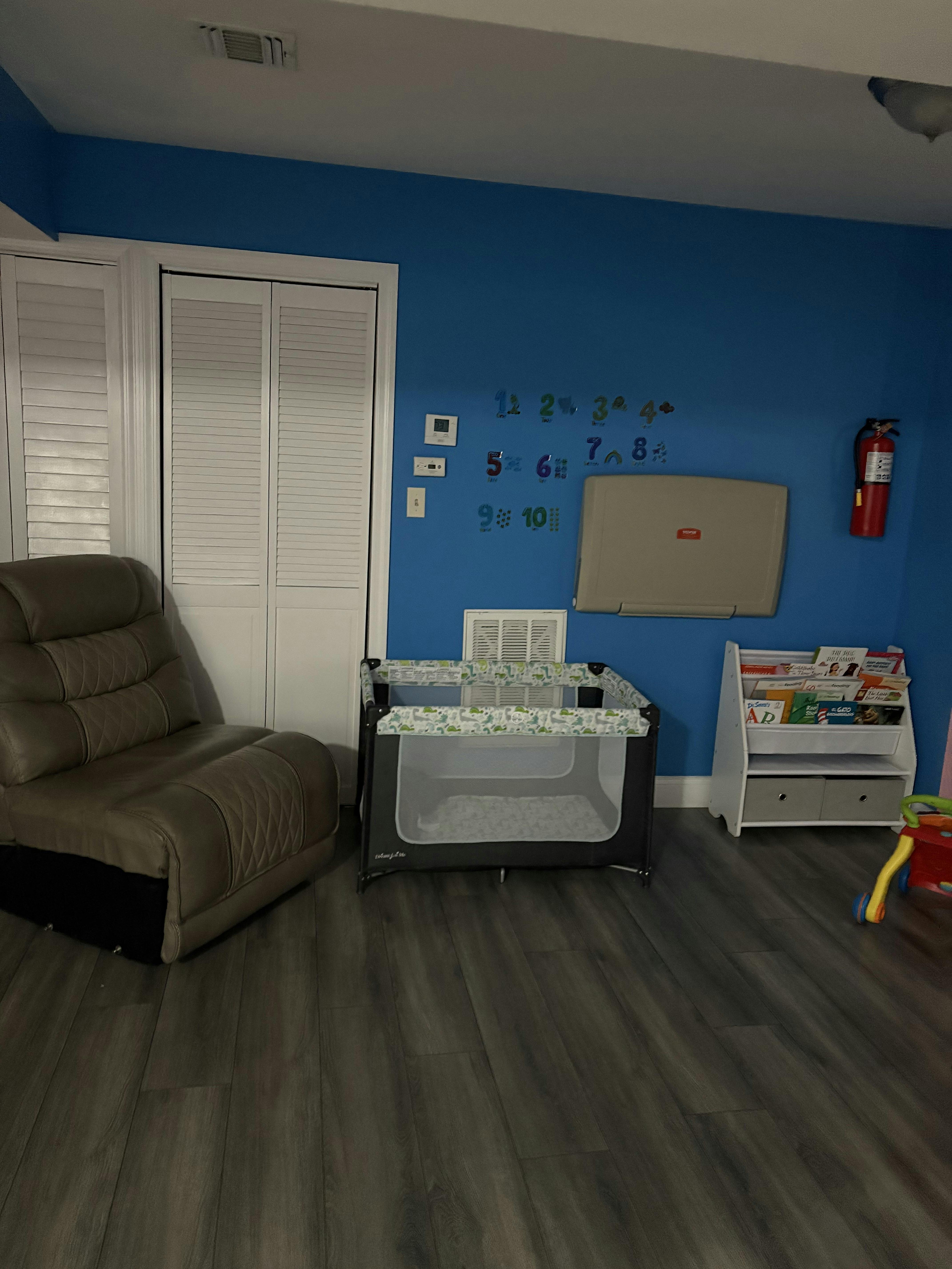 A playroom with a playpen, a chair, and a bookshelf