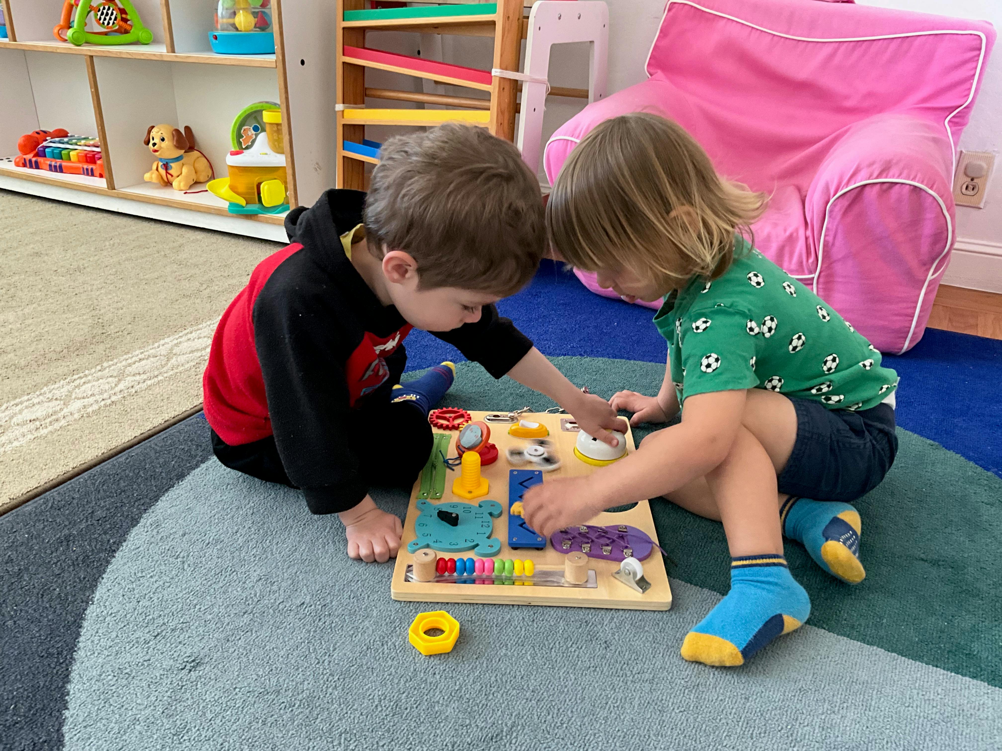 Two children sitting on a rug and playing with a wooden sensory board