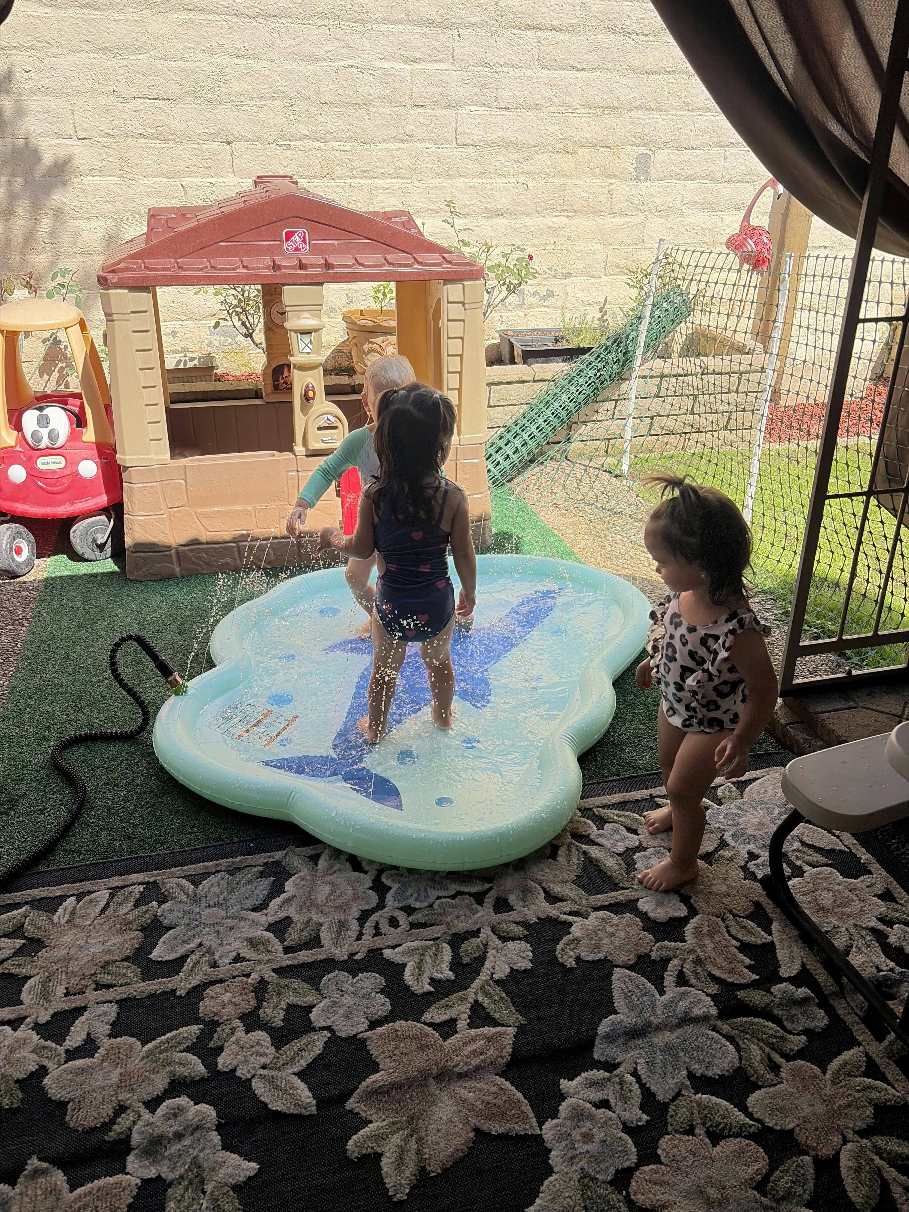 Three children playing in a backyard splash pad