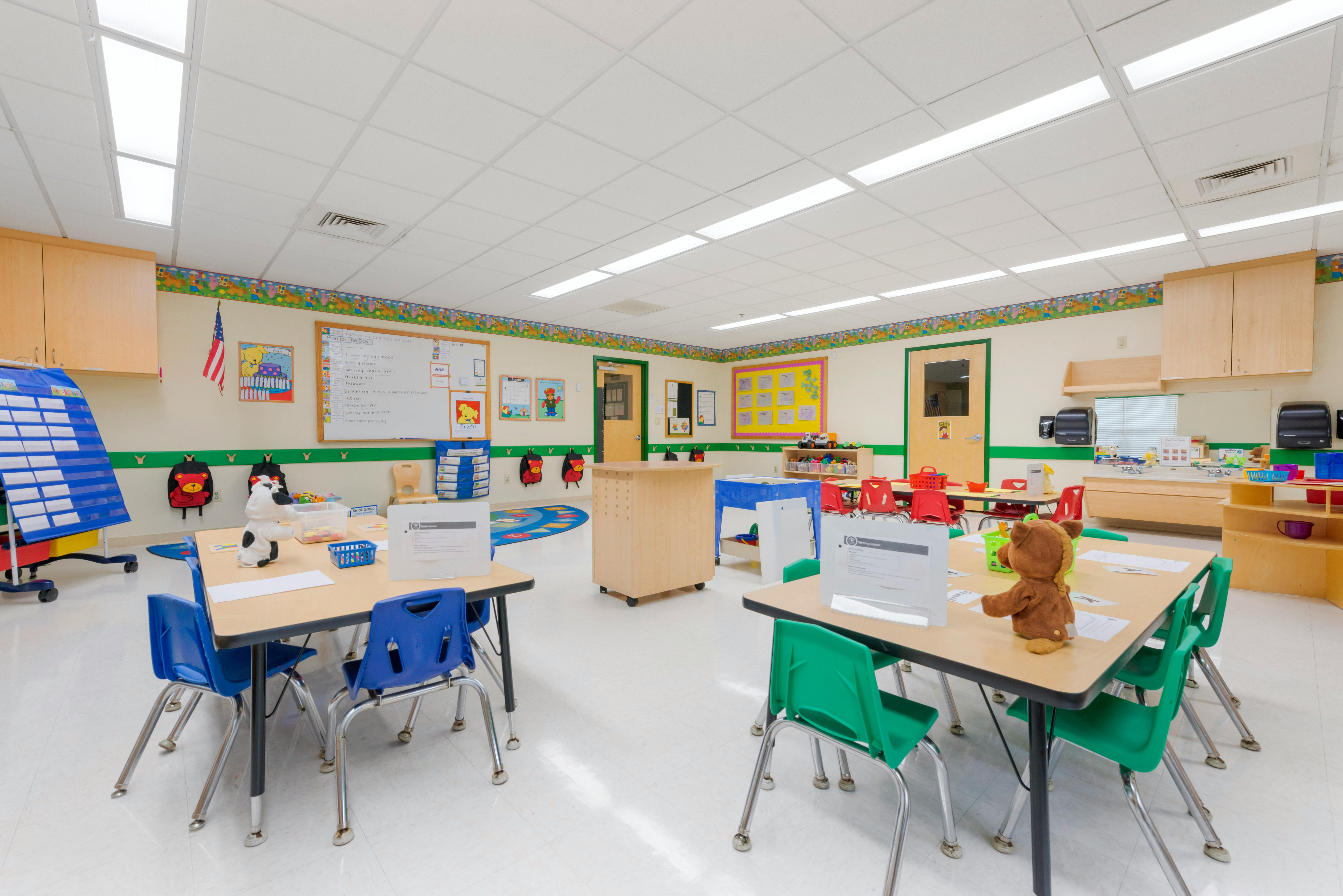 Empty classroom with small tables and chairs, whiteboards, and cubbies