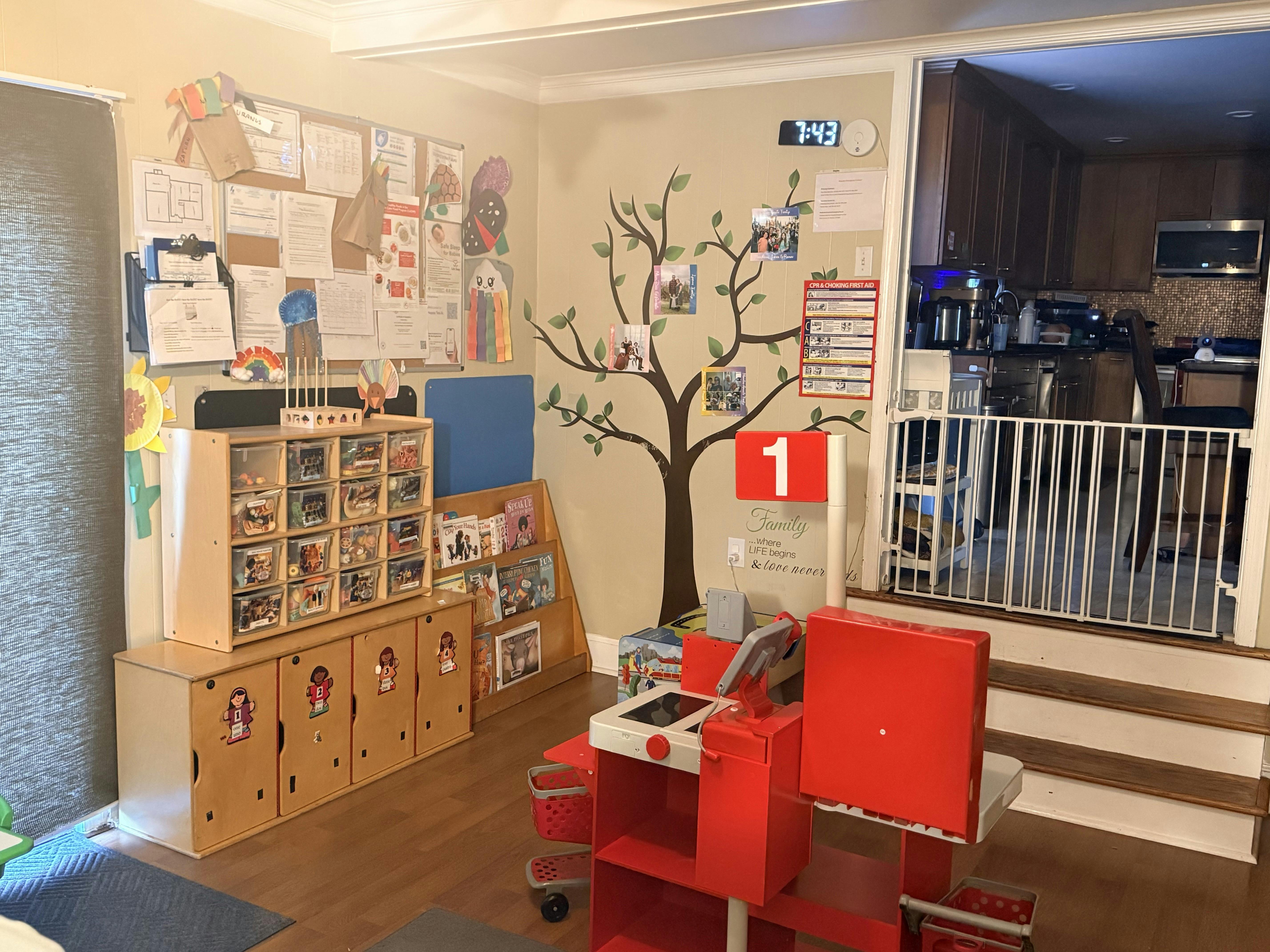 Playroom with a storage unit, bookshelf, tree decal, toy cash register, and baby gate