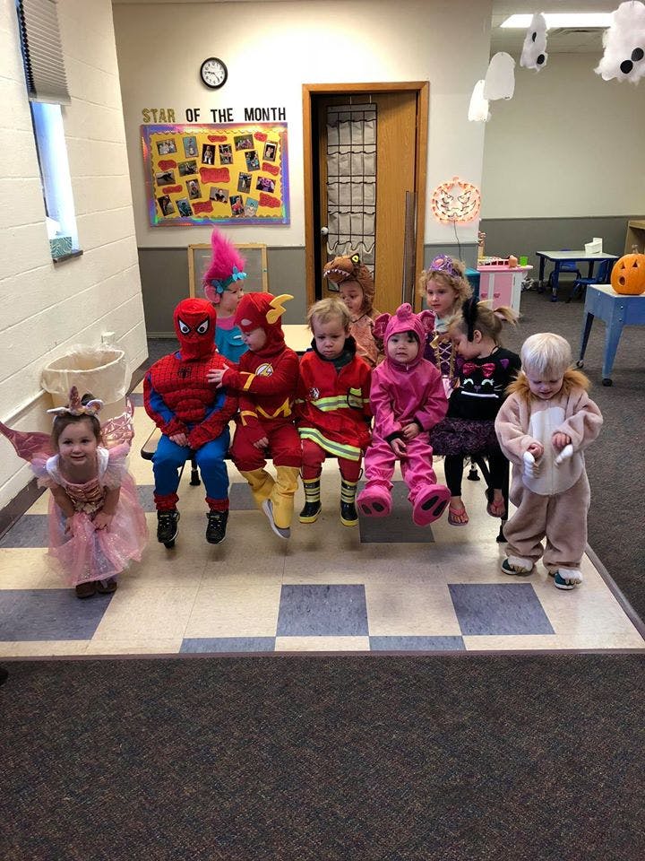 Children in costumes sitting on a bench in a classroom