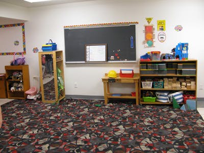 Classroom with a chalkboard, shelves of toys, and patterned carpet