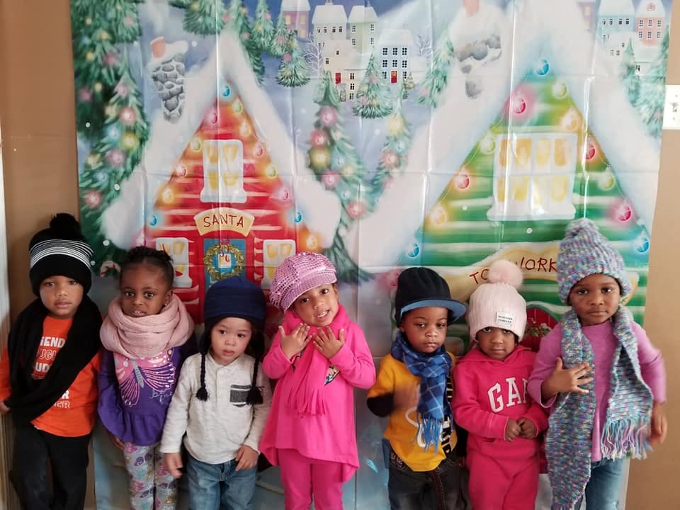 Six children in winter hats and scarves in front of a winter scene backdrop