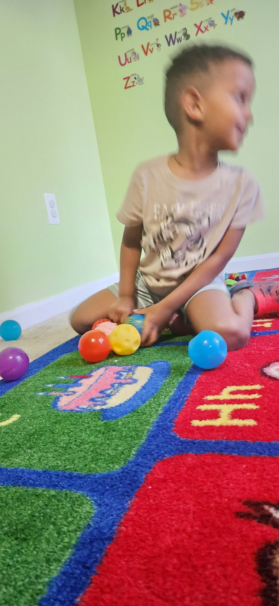 Child sitting on a colorful rug with several balls
