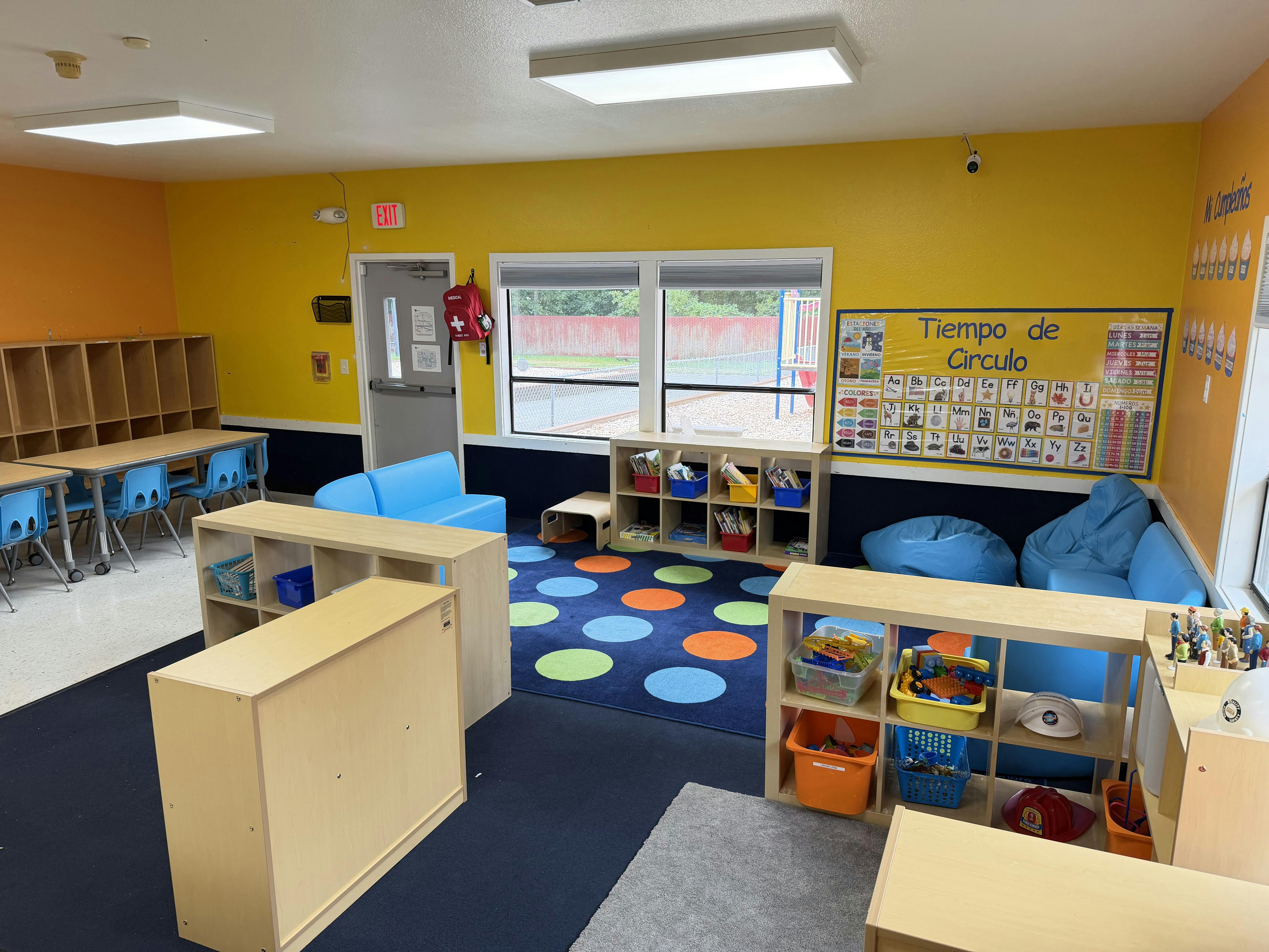 Classroom interior with tables, shelving units, blue beanbags, and a rug
