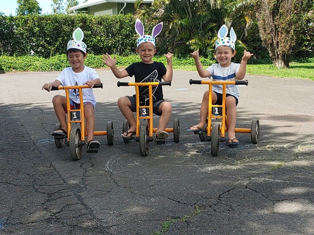 Three children wearing bunny ears riding tricycles
