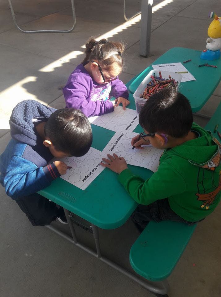 Three children drawing at a picnic table