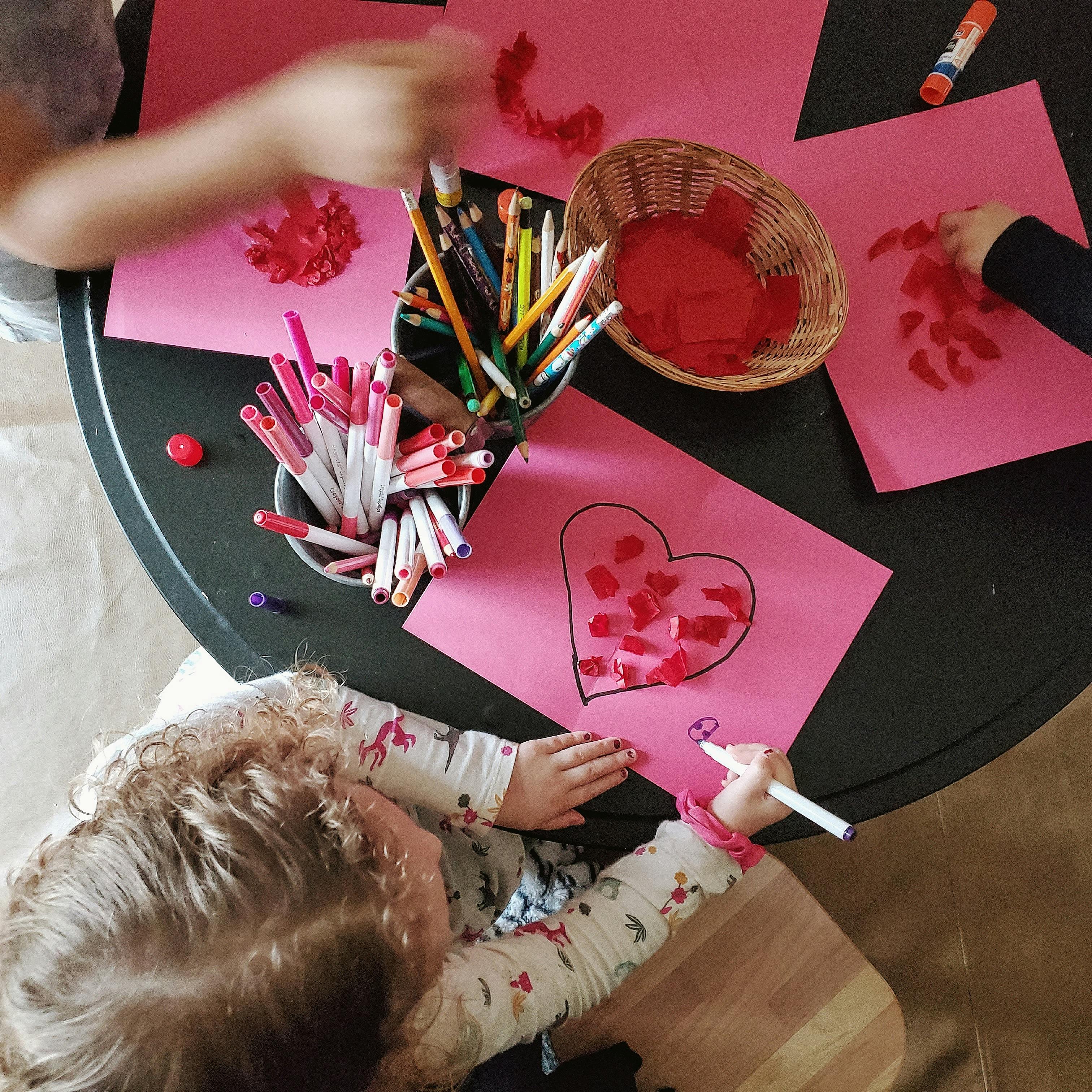 Children doing crafts with pink paper and red materials
