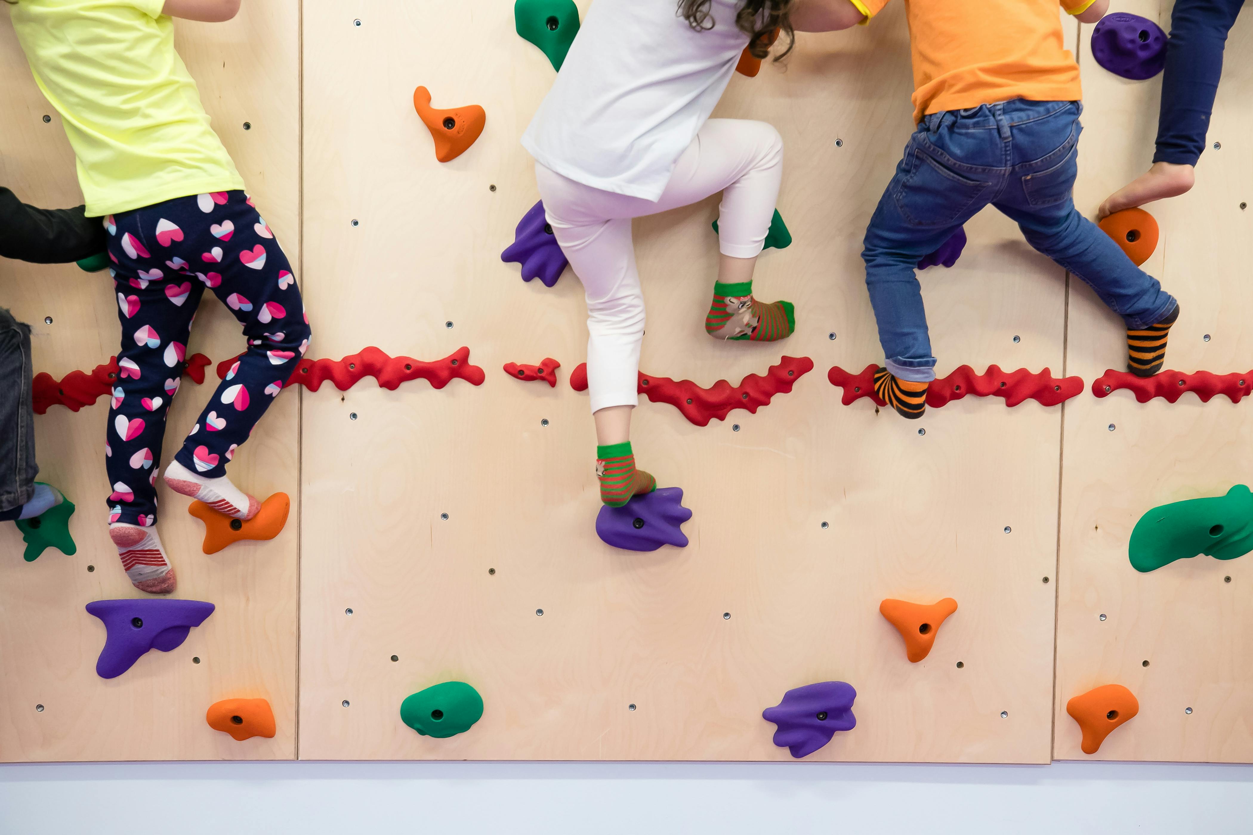 Multiple children climbing a wooden rock-climbing wall with colorful holds