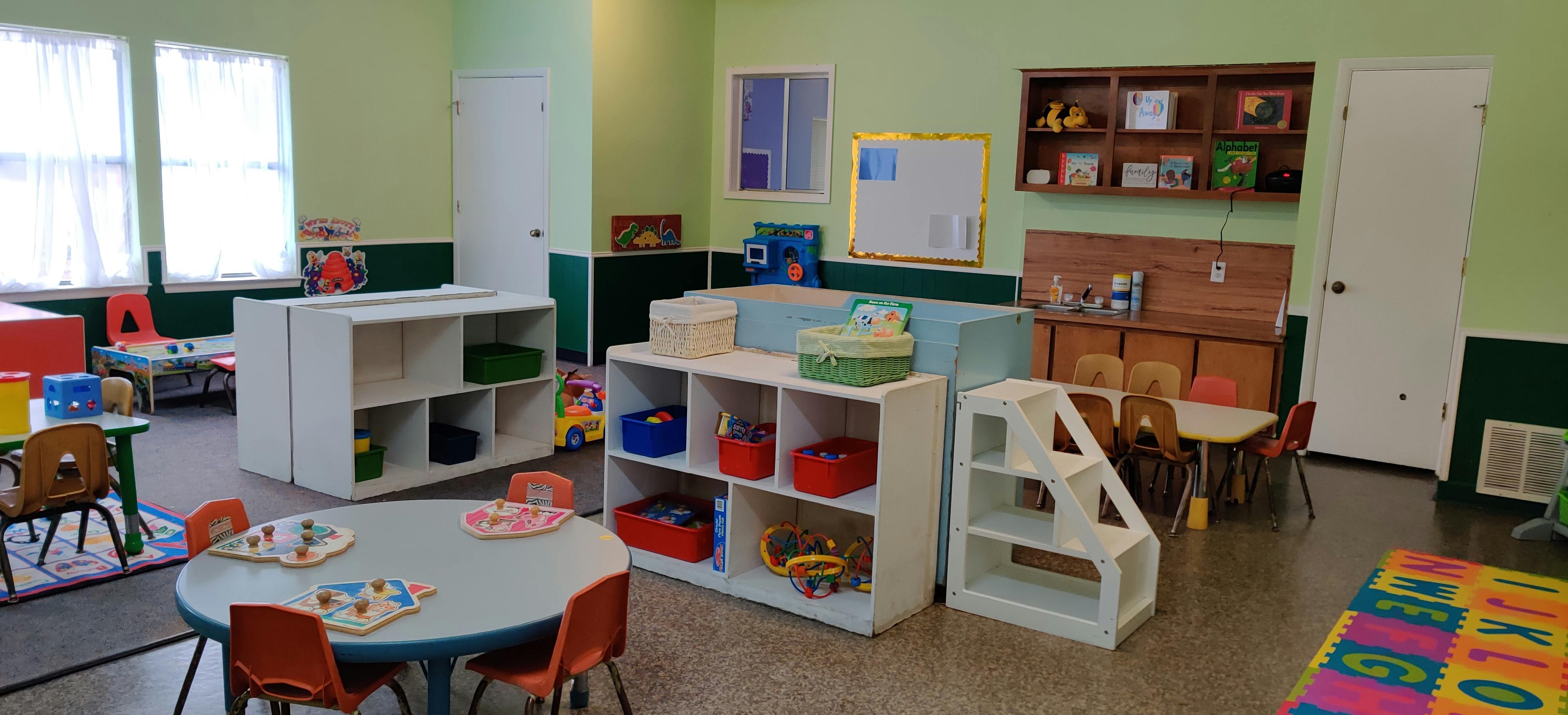 Classroom with small tables and chairs, shelves with toys and books