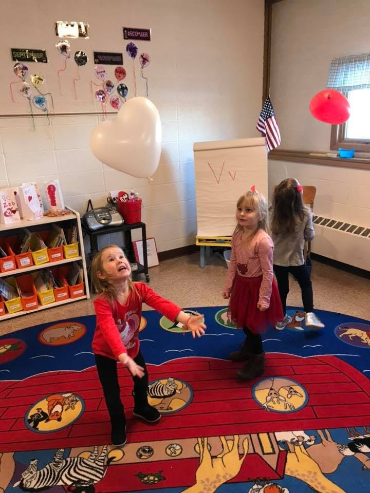 Child reaching for a heart-shaped balloon in a classroom