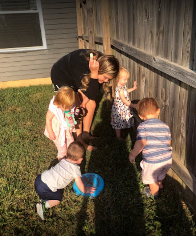 Person with three children and one toddler in a grassy area