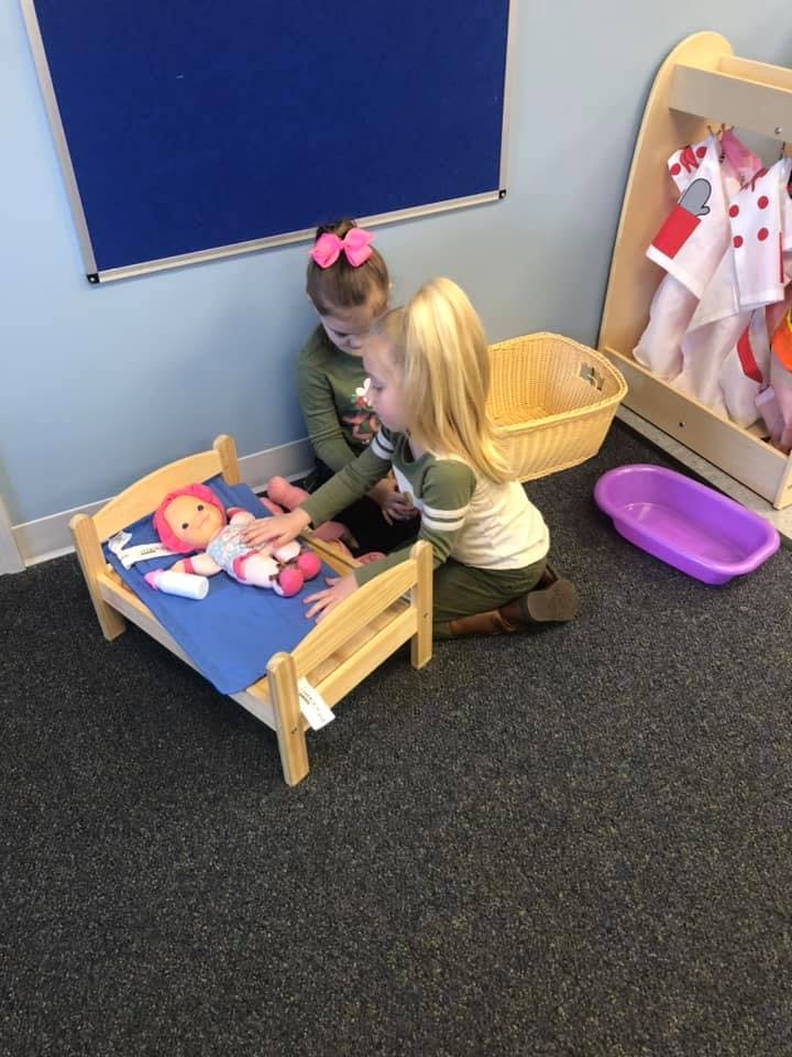 Two children playing with a doll in a toy bed