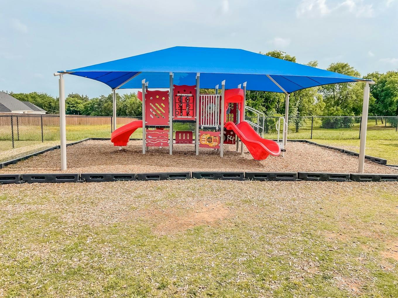 Playground structure with two slides under a large blue shade canopy