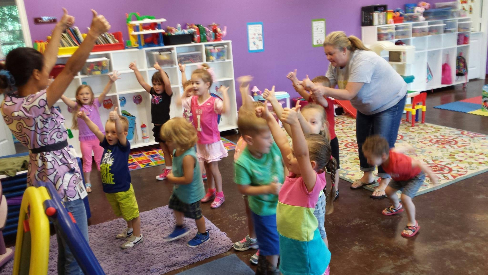 Adults and children with arms raised in a classroom