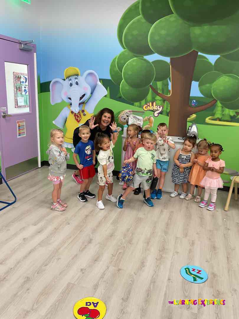 Adult and children posing with a cartoon elephant cutout in a classroom