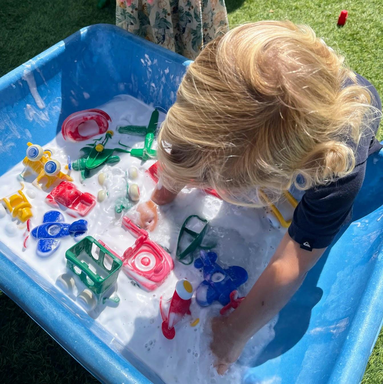 Child playing with plastic toys in a sensory bin filled with soapy water