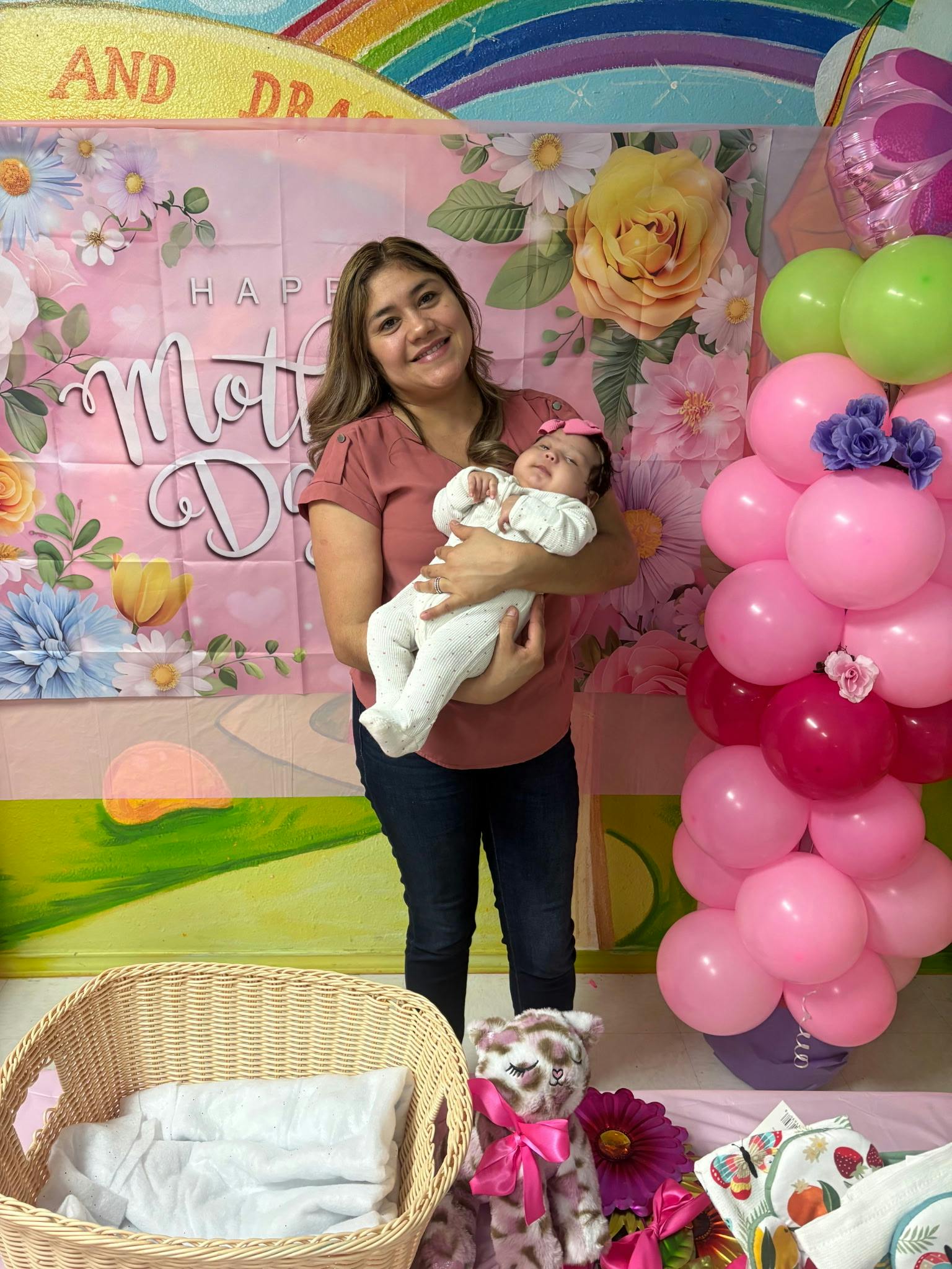 Person holding a baby in front of a Mother's Day floral backdrop