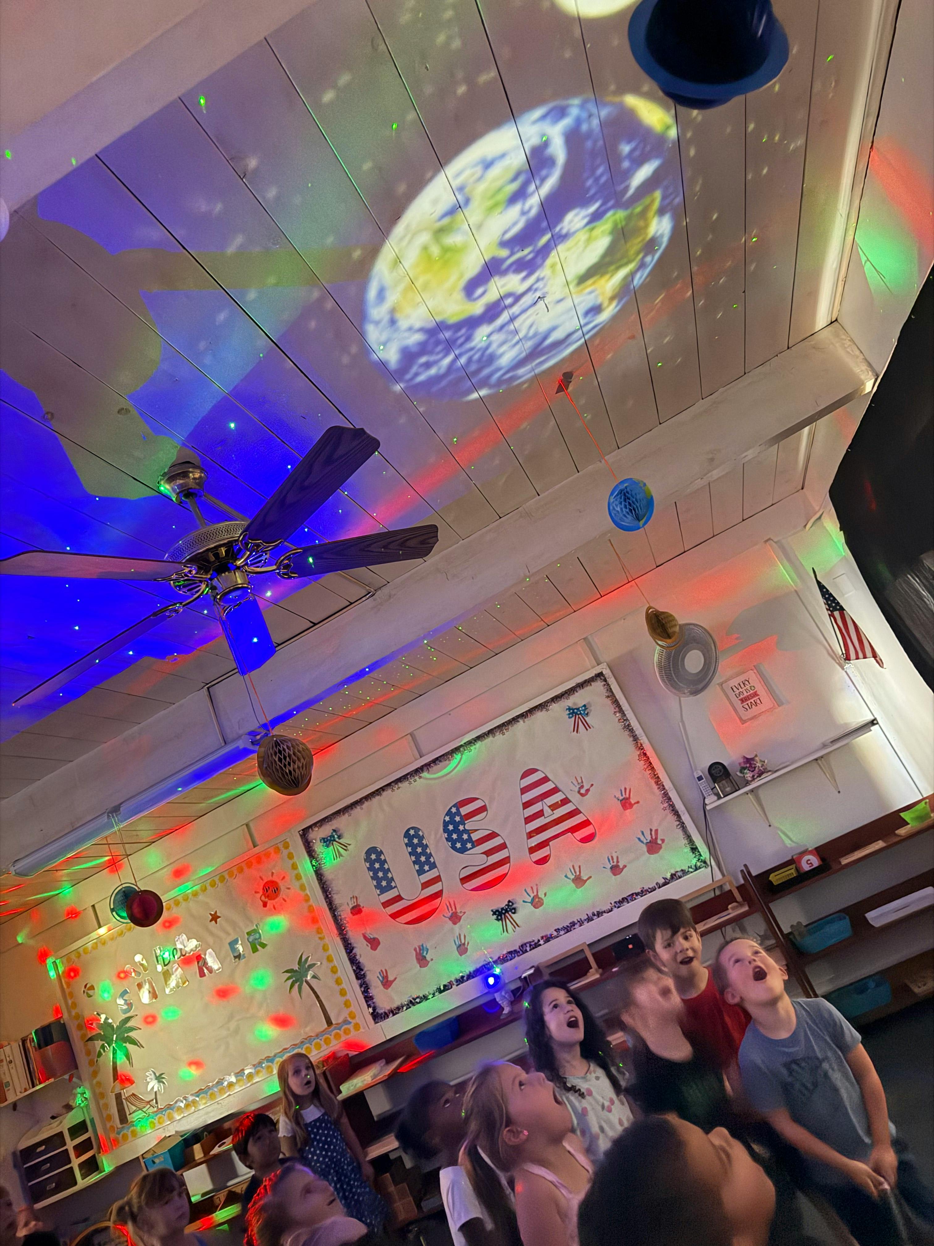 Group of children looking up at a ceiling with projected lights and decorations