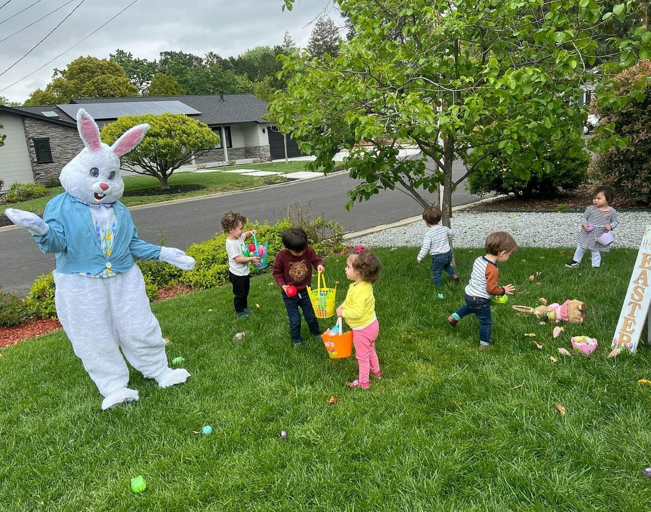 Person in a bunny costume with children holding baskets on grass