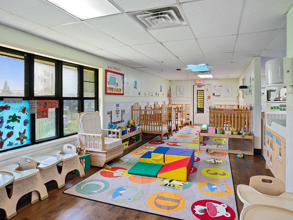 Baby room with multiple cribs, a colorful rug, and child-sized furniture