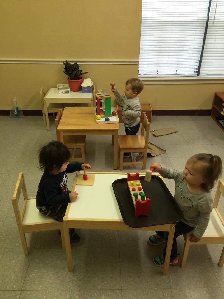 Three children playing with toys at small tables in a classroom