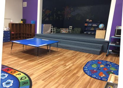 Classroom with a blue table, wooden floor, and a raised stage area