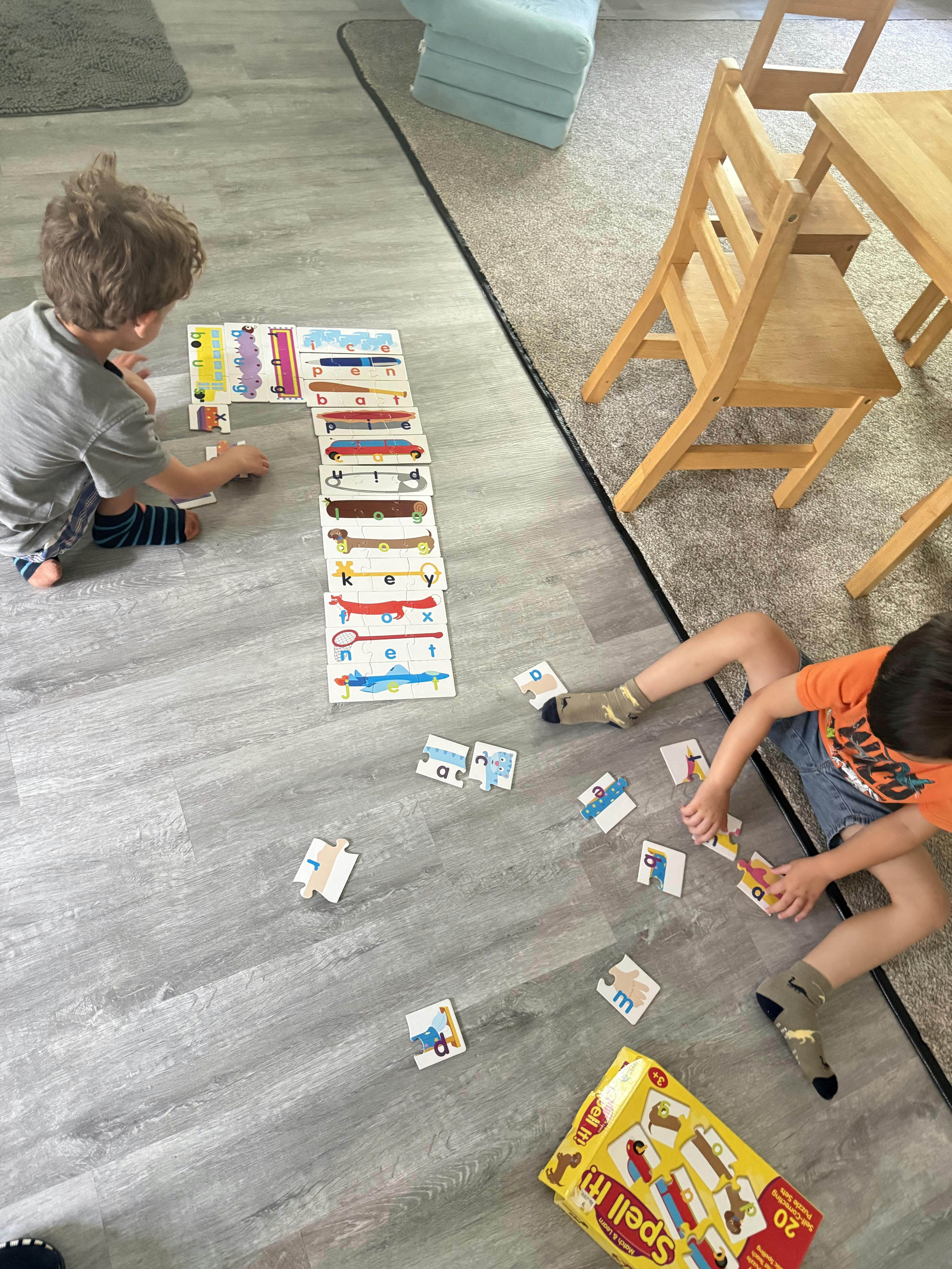 Two children sitting on the floor assembling spelling puzzle cards