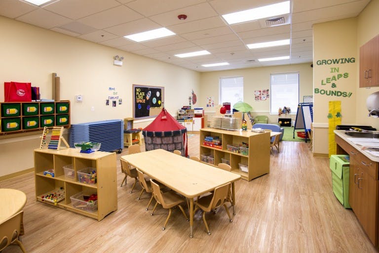 Empty classroom with tables, chairs, and shelves with toys