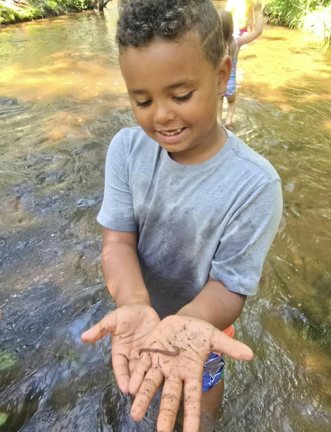 Child in a creek holding an earthworm in cupped hands