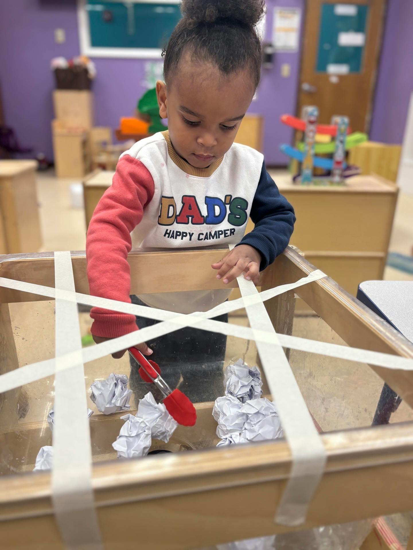 Child using tongs to pick up crumpled paper in a sensory bin