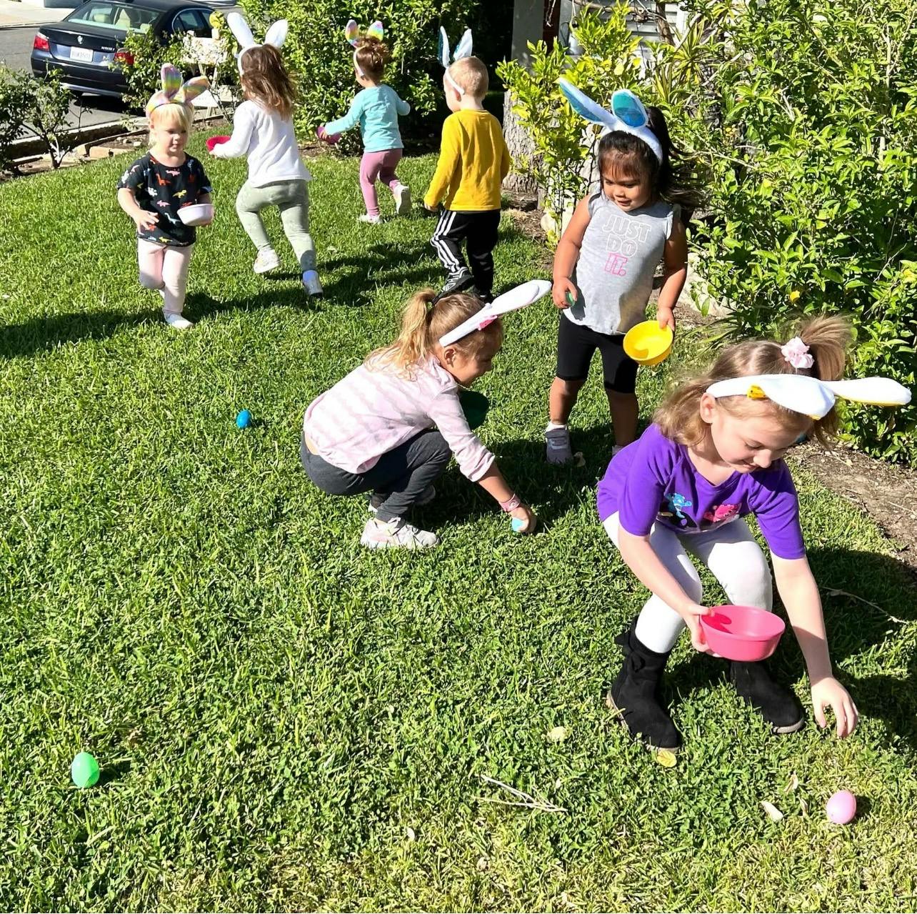 Children wearing bunny ears collecting Easter eggs on a lawn