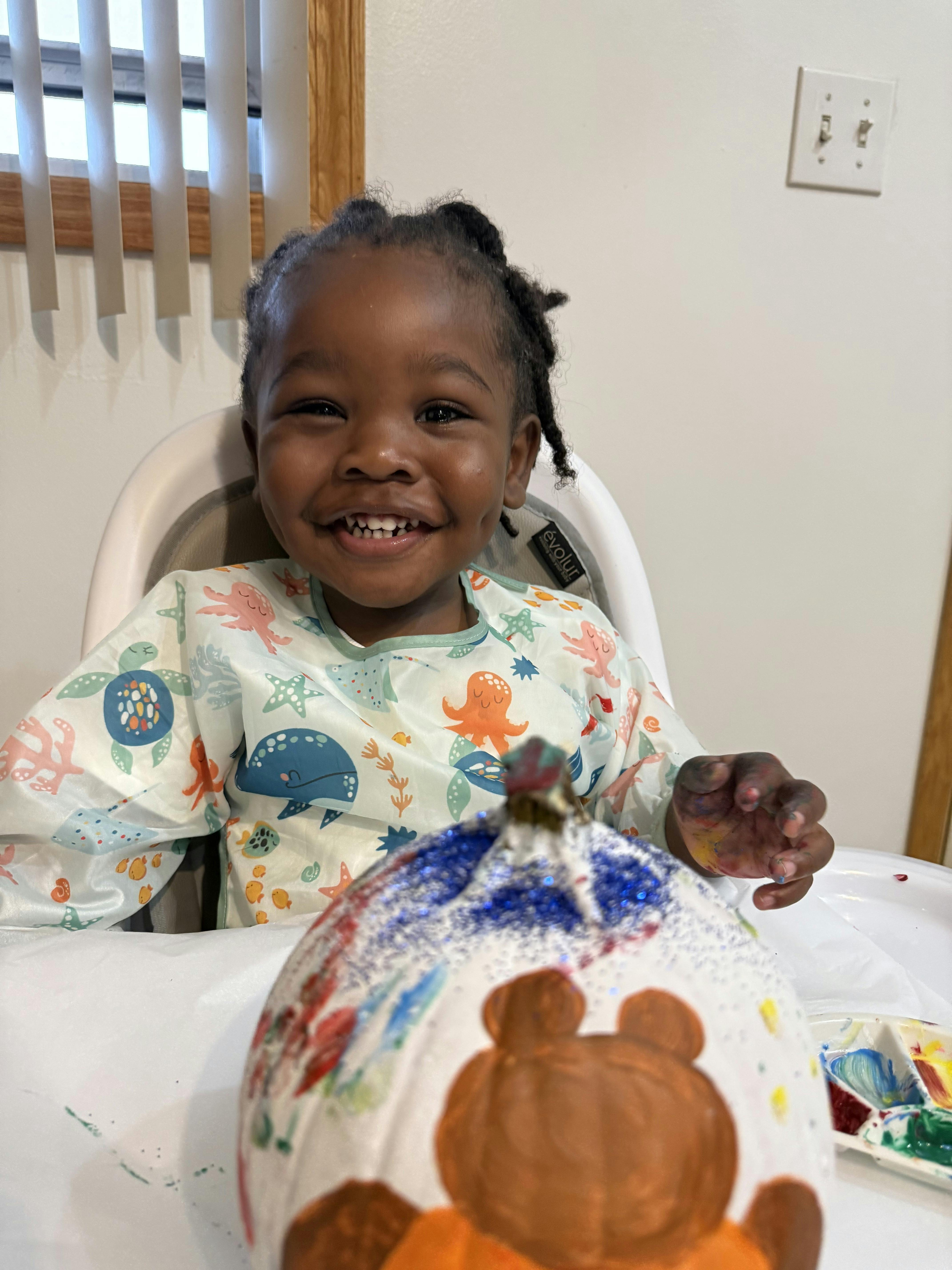 Child in a high chair painting a pumpkin