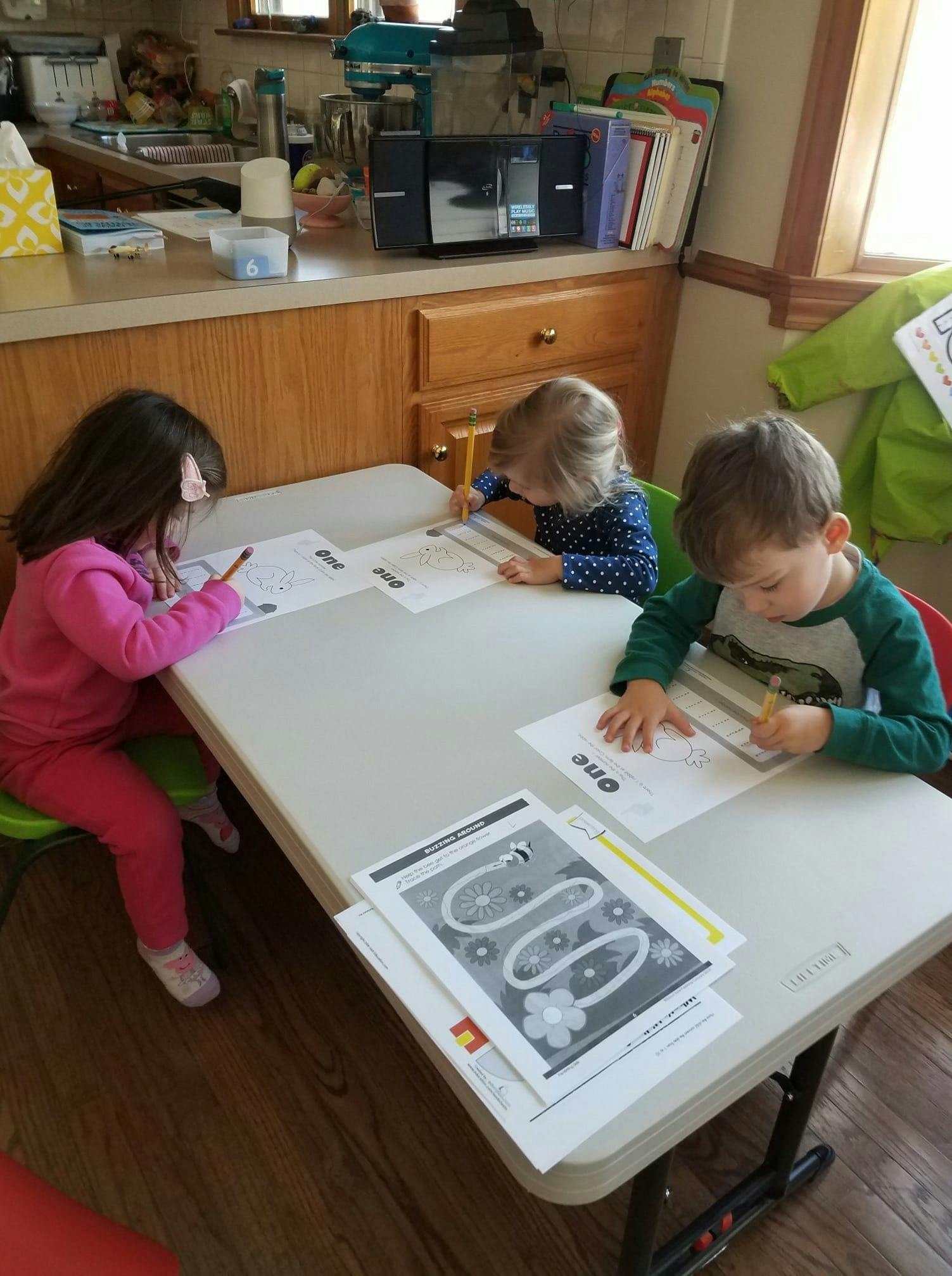 Three children drawing and writing at a table