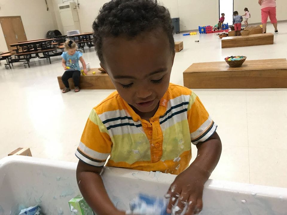 Child playing with foam in a white tub