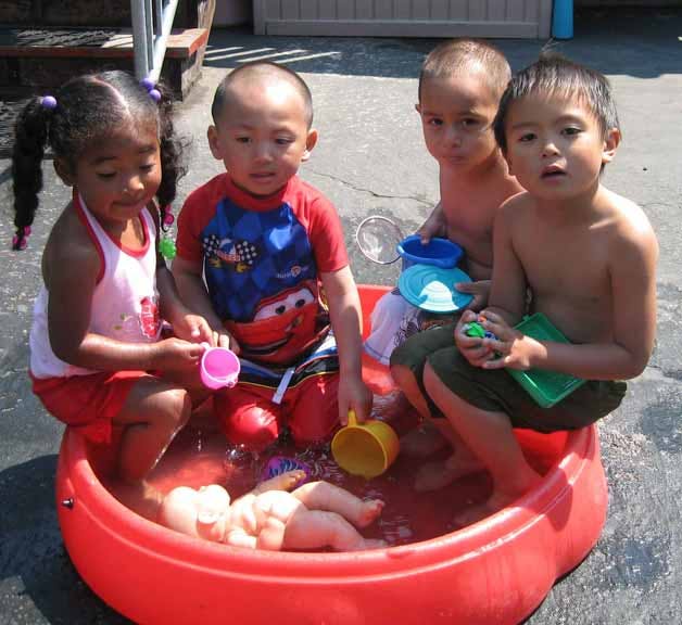 Four children playing in a red plastic pool with water and toys
