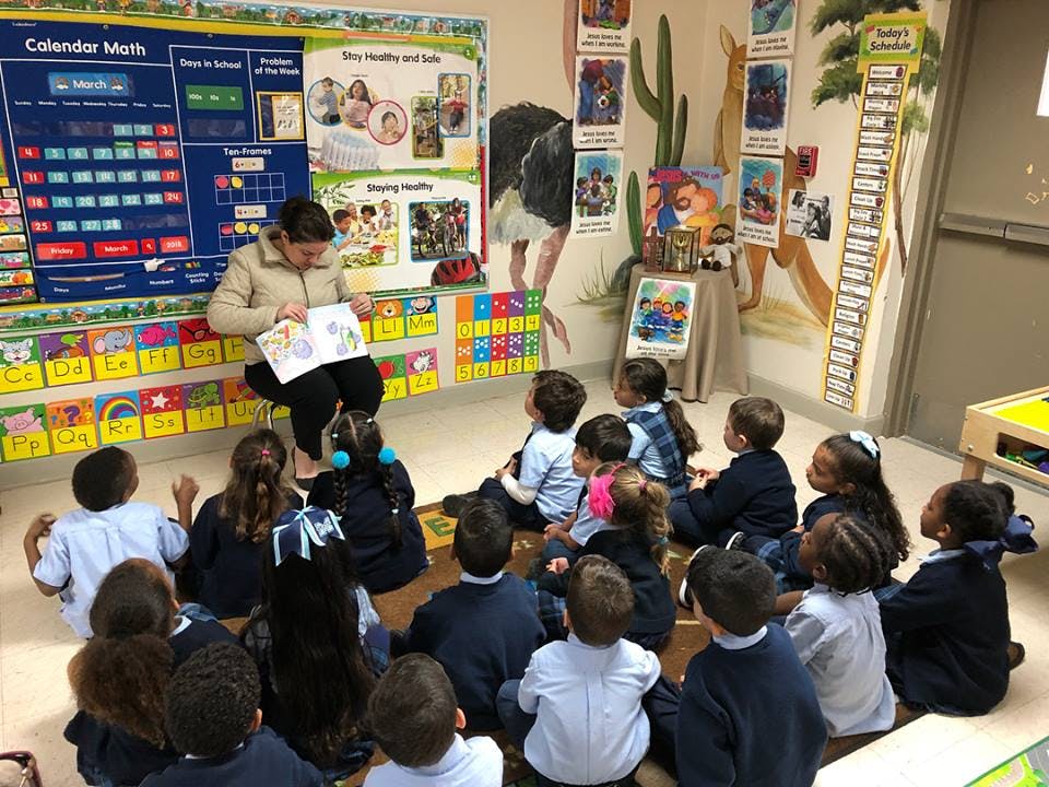 Person reading a book to a group of children in a classroom