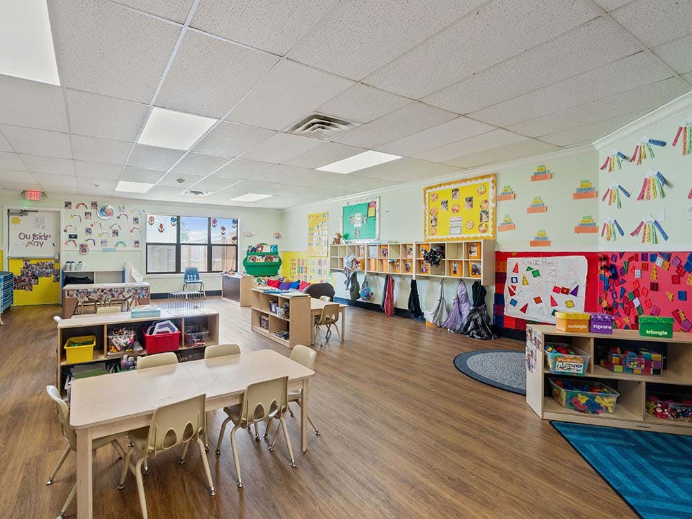 Empty classroom with small tables and chairs, cubbies, and colorful decorations