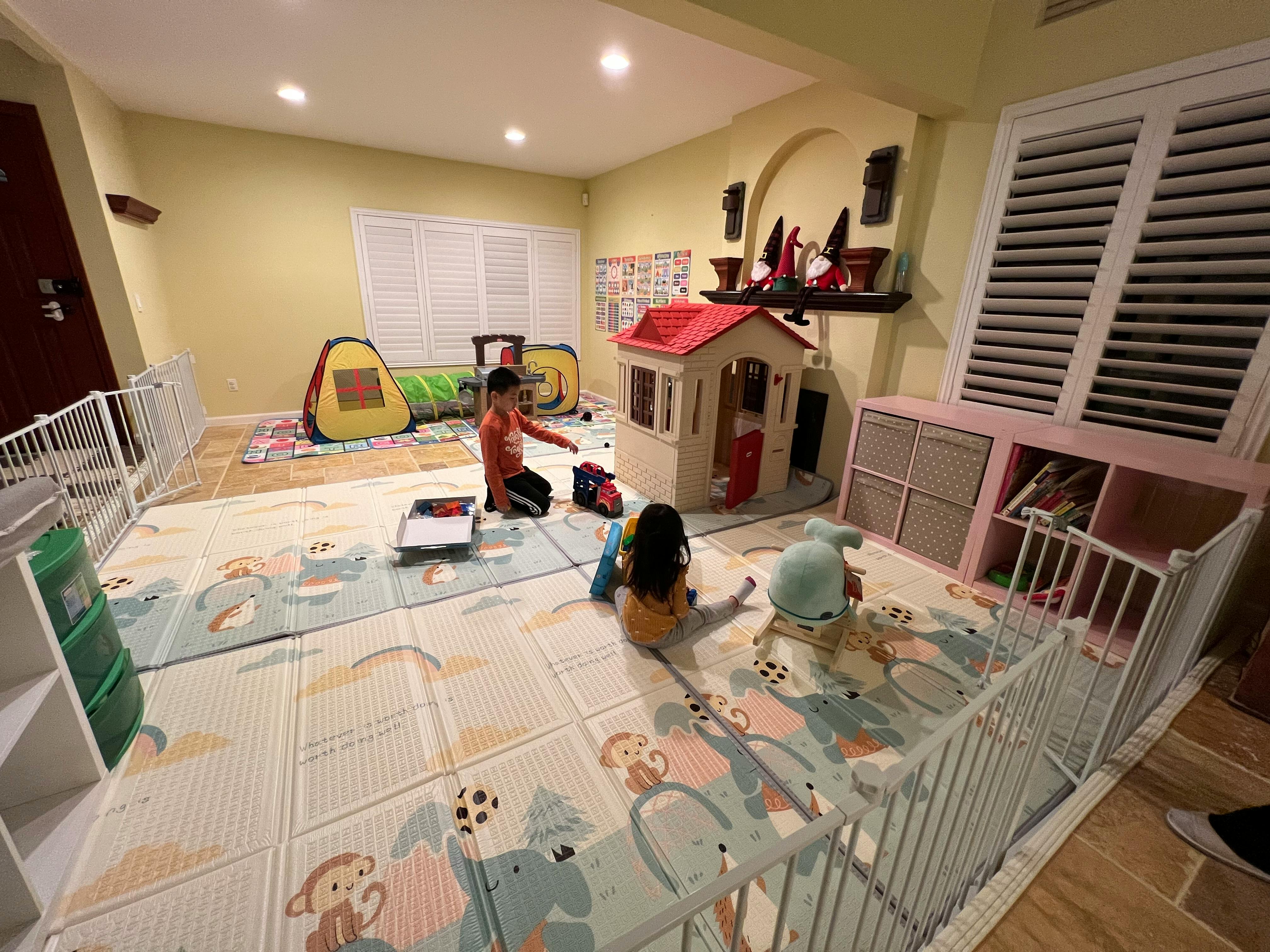 Two children playing on a mat in a room with a playhouse
