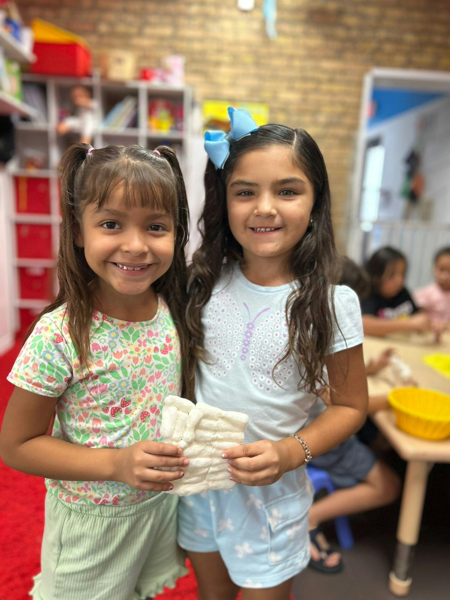 Two children holding a white knitted item in a classroom