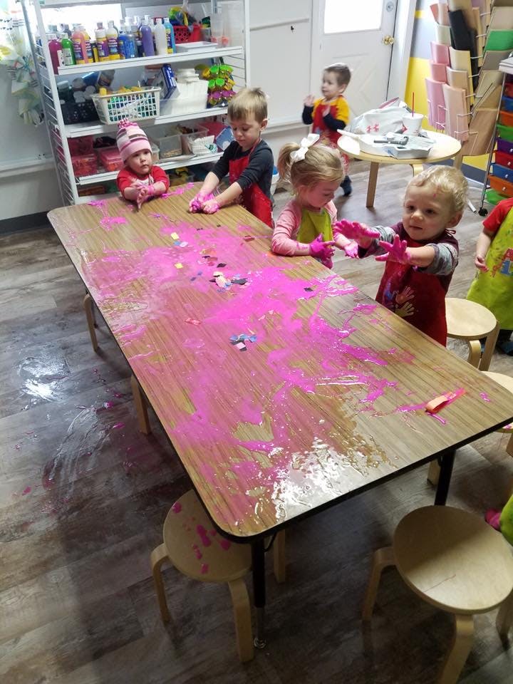 Children playing with pink paint on a table in a classroom